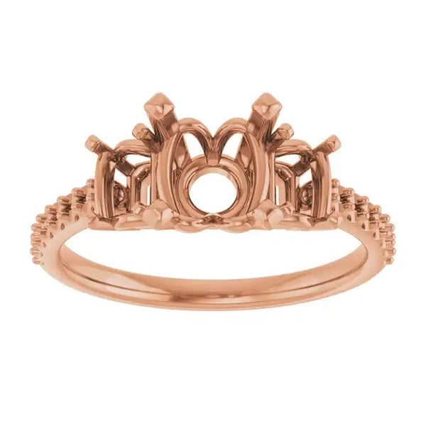 Rose gold engagement ring setting with ornate crown-style head and textured band for round stone placement.