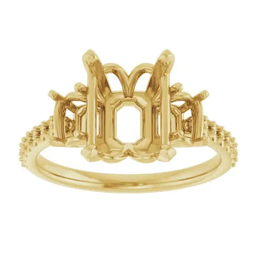 Gold engagement ring setting with ornate emerald-cut stone holder, decorative side accents, and textured band.