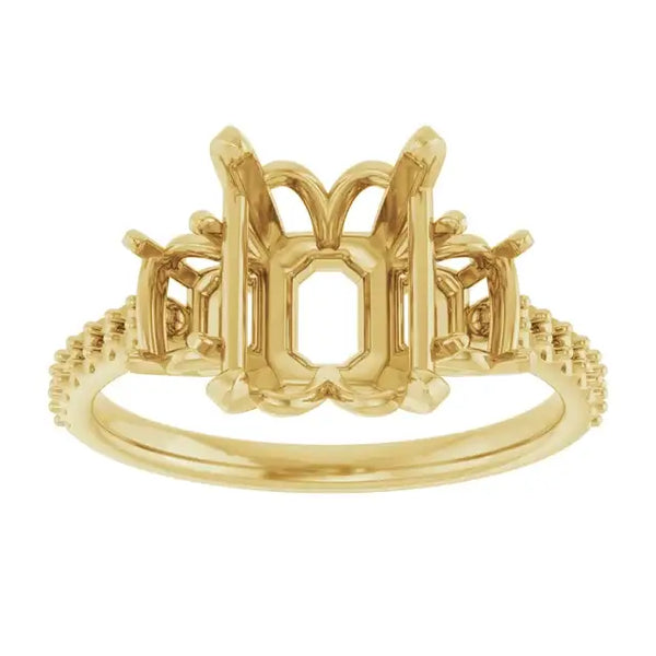 Gold engagement ring setting with ornate emerald-cut stone holder, decorative side accents, and textured band.