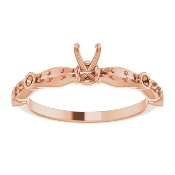 Rose gold engagement ring setting with ornamental prongs and studded band for emerald stone.