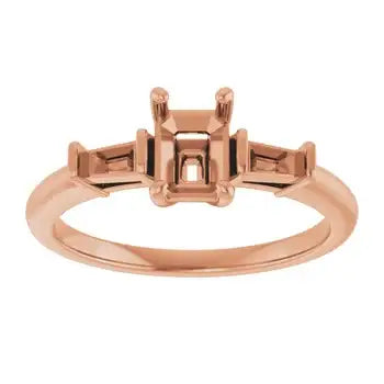 Rose gold engagement ring setting with emerald-cut stone holder and rectangular side stone settings.
