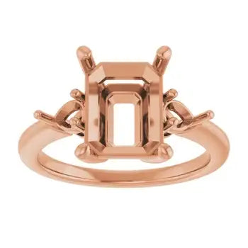 Rose gold engagement ring setting with empty emerald-cut stone holder and decorative side accents.
