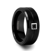 ATLAS black tungsten carbide ring, 9 mm wide, with brushed center, polished beveled edges, grooved center line, and a 0.1 ct round black diamond set in a square bezel, angled view