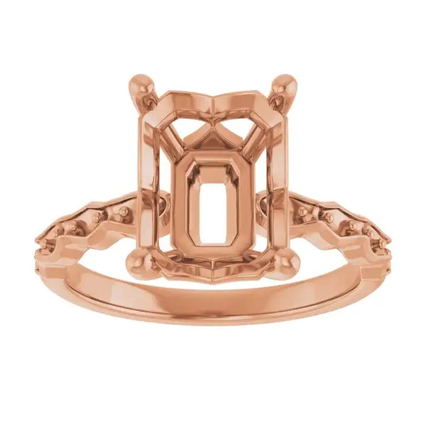 Rose gold French-set engagement ring setting with emerald-cut center stone housing and decorative side details.