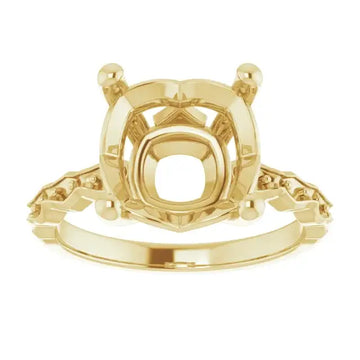 Gold engagement ring setting with cushion-cut stone mounting, decorative side accents, and prong-style head.