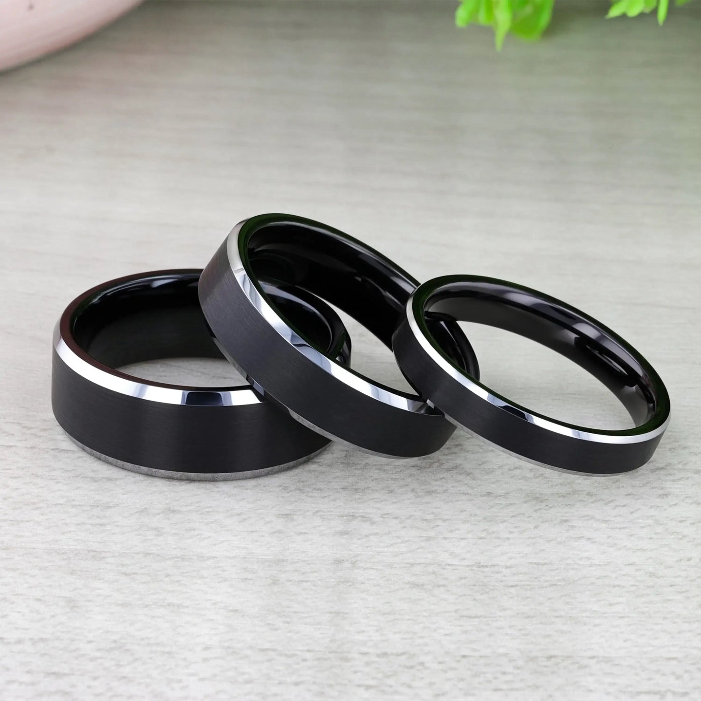 Lifestyle image of black brushed-center tungsten ring with polished beveled edges on dark background