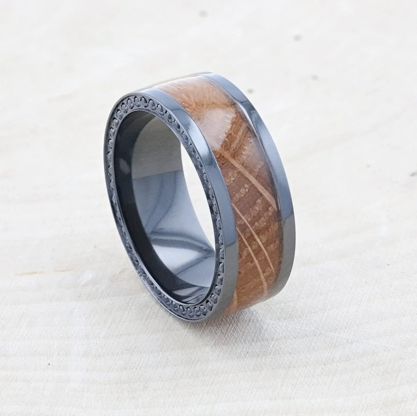 Lifestyle angled shot of the ring on a light wood surface, showing the whiskey barrel grain and black sapphire rim detail.