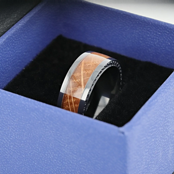 Ring displayed in a blue gift box, emphasizing the polished whiskey barrel wood inlay and glossy black zirconium edges.