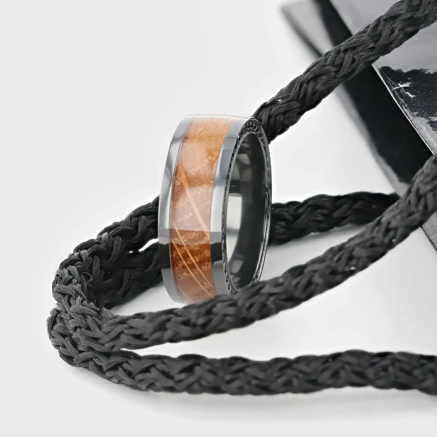 Close-up lifestyle shot of the ring resting on black braided cords, showcasing the wood inlay and black sapphire accent edge.