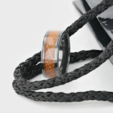 Close-up lifestyle shot of the ring resting on black braided cords, showcasing the wood inlay and black sapphire accent edge.