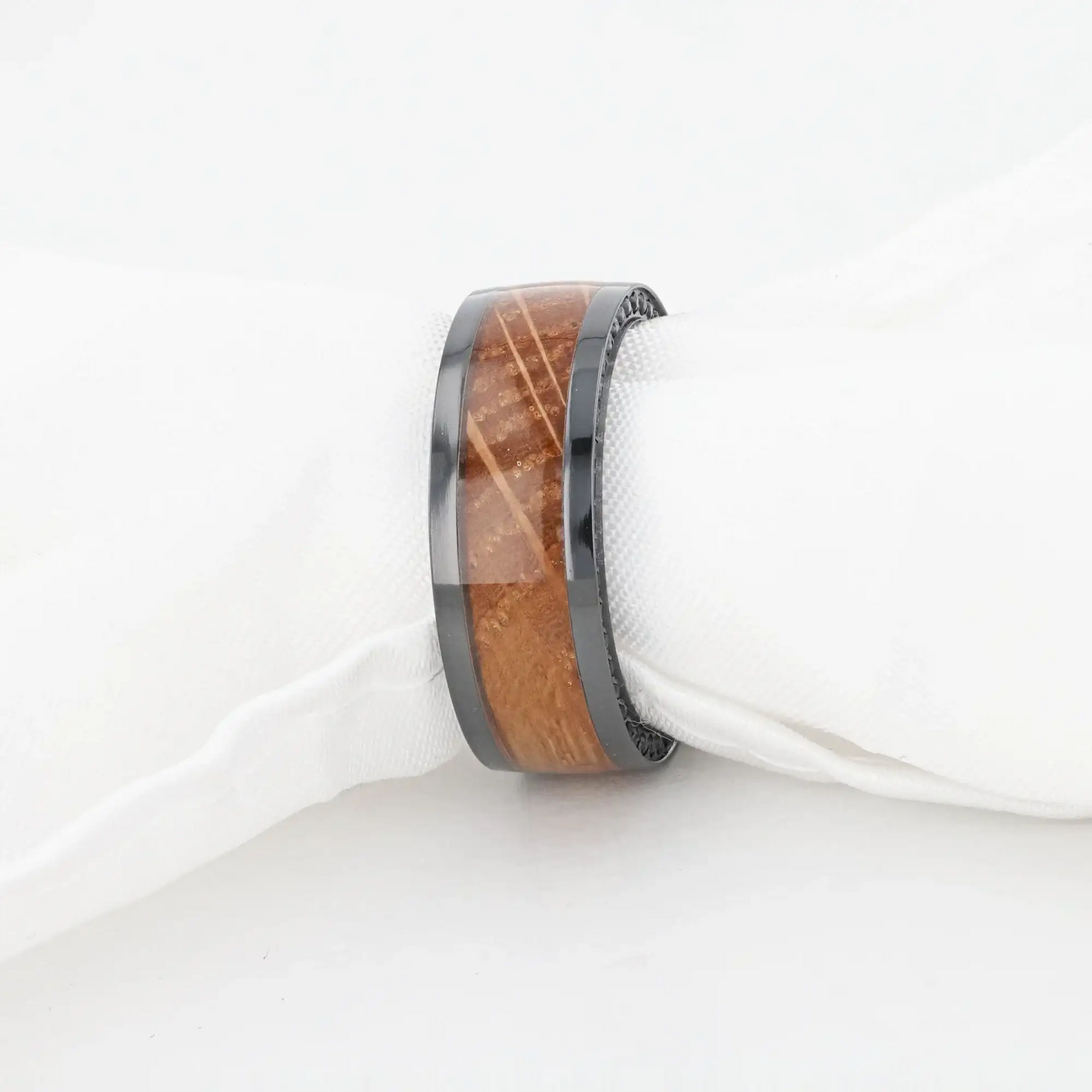 Ring wrapped around a white cloth napkin to demonstrate scale, with the whiskey barrel wood inlay and black zirconium edges visible.