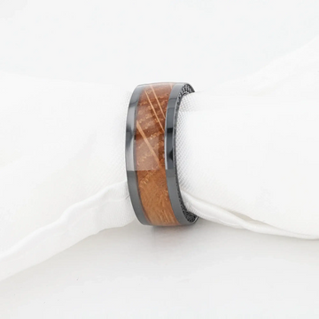 Ring wrapped around a white cloth napkin to demonstrate scale, with the whiskey barrel wood inlay and black zirconium edges visible.