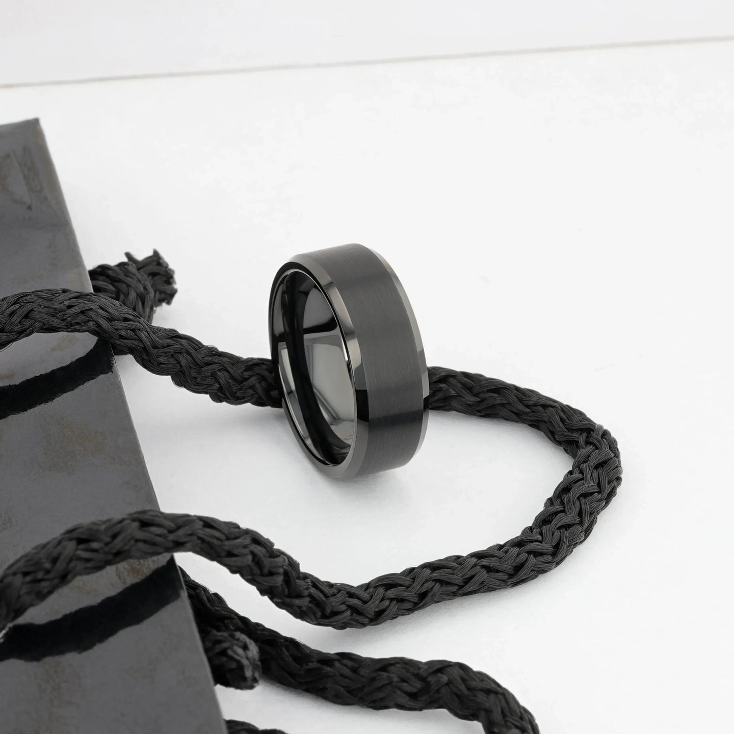 Black brushed tungsten ring resting on a braided black cord