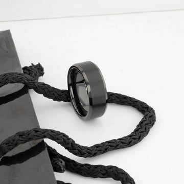 Black brushed tungsten ring resting on a braided black cord