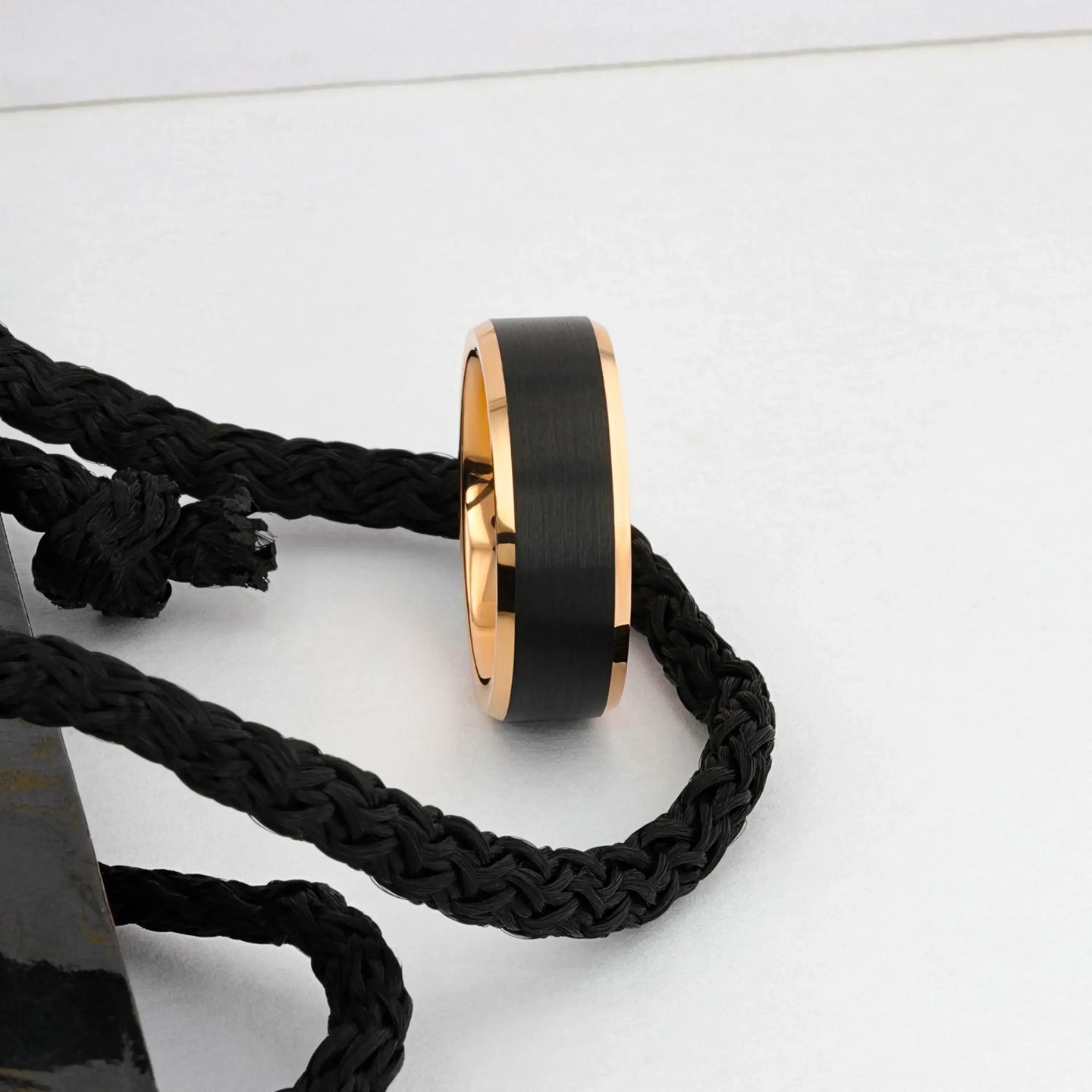Rose gold and black tungsten ring styled next to a black braided cord, side view