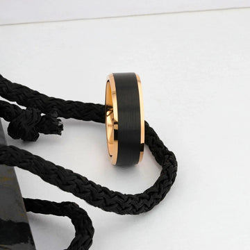 Rose gold and black tungsten ring styled next to a black braided cord, side view