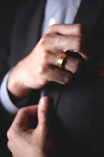 Two gold-plated tungsten rings side by side on a braided cord, one wide and one narrow, both with brushed centers.