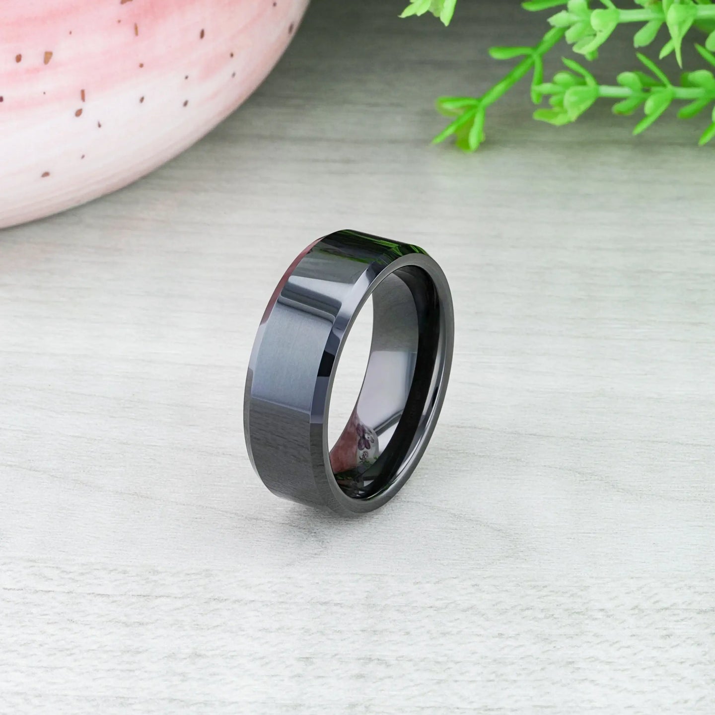 Studio shot of the INFINITY black tungsten ring with beveled edges on a reflective surface