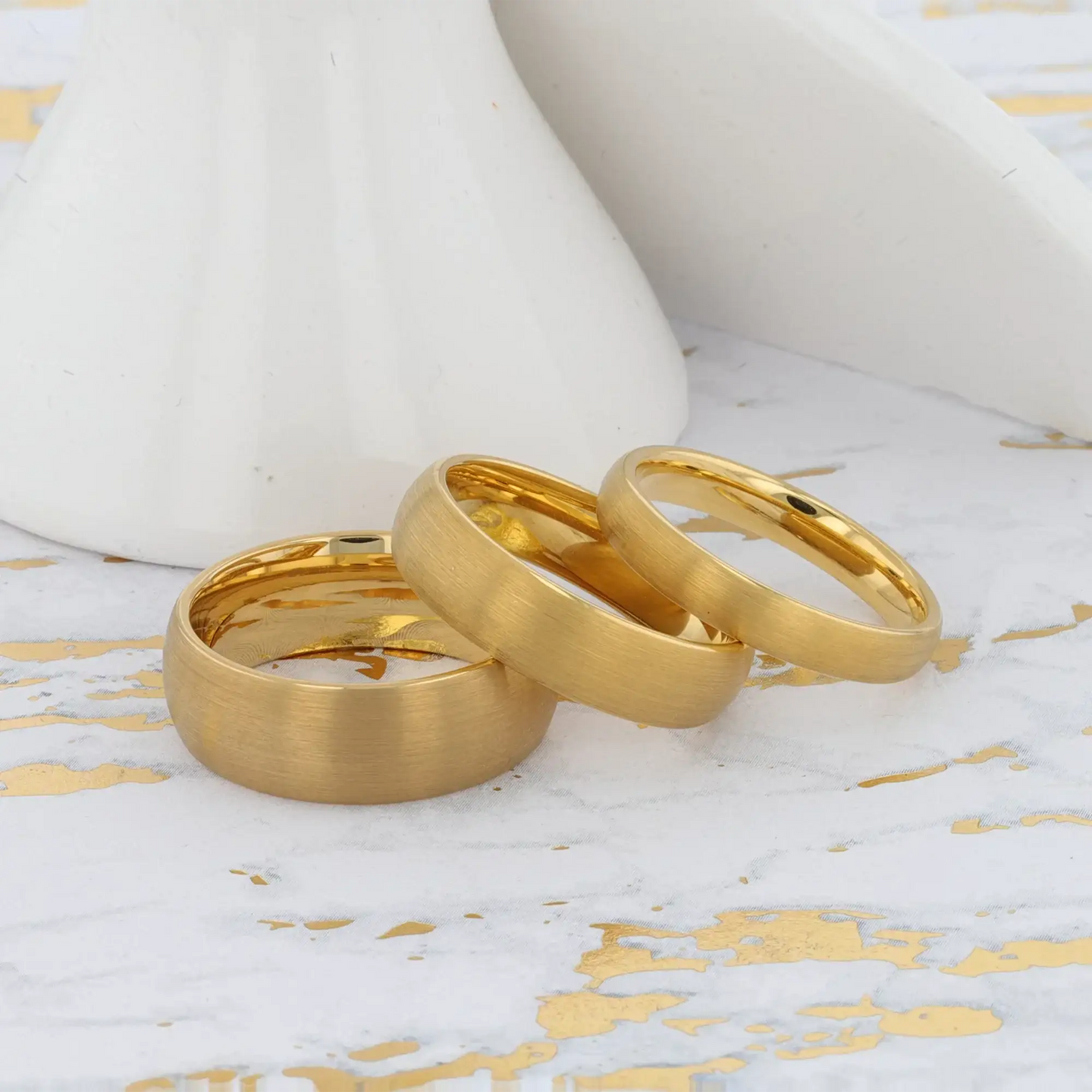 Set of three brushed gold-plated tungsten rings arranged on a metallic background