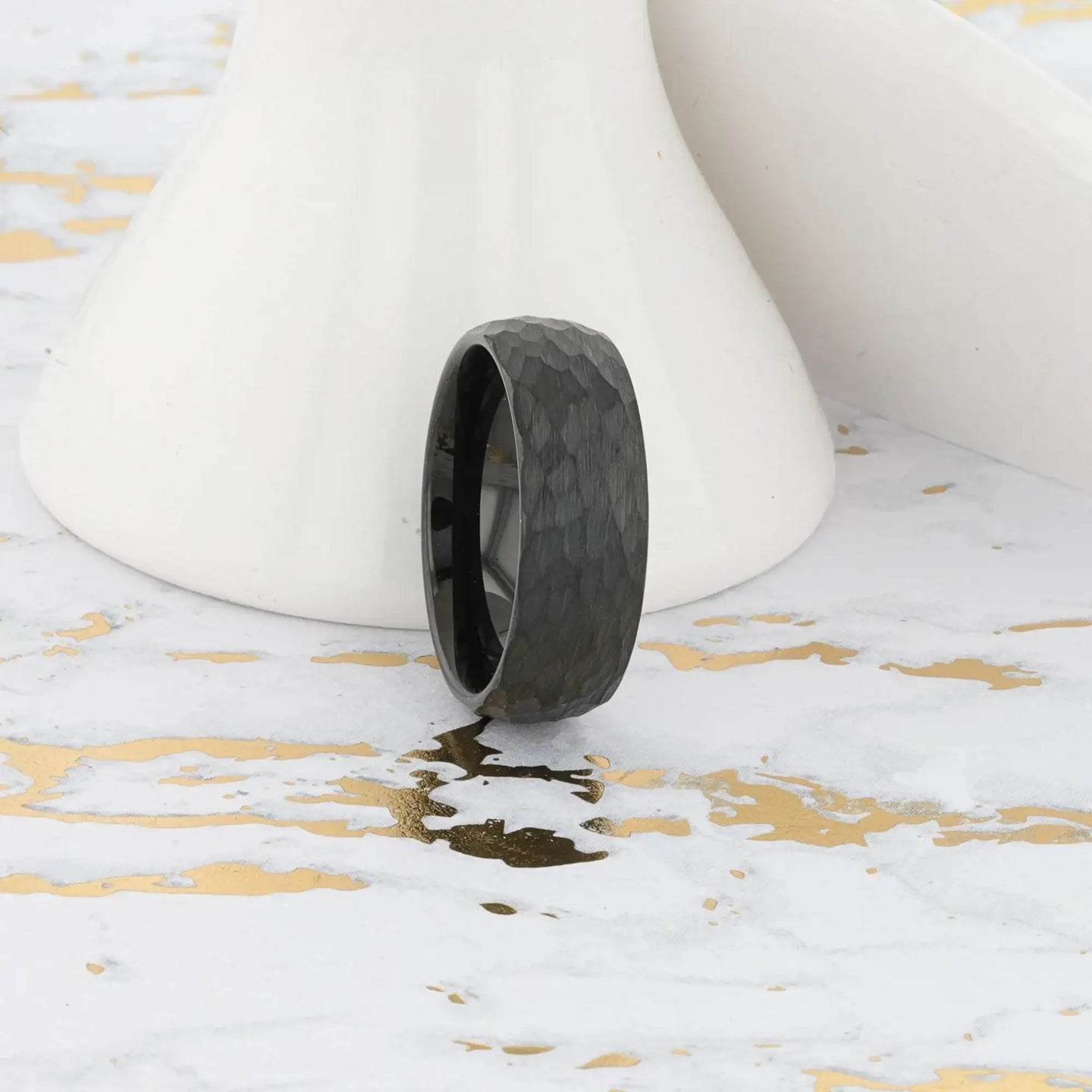 Lifestyle image of the RENEGADE hammered black tungsten carbide ring against white and gold background