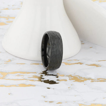 Lifestyle image of the RENEGADE hammered black tungsten carbide ring against white and gold background