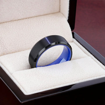 Black tungsten ring with bright blue interior displayed in a cream jewelry box.