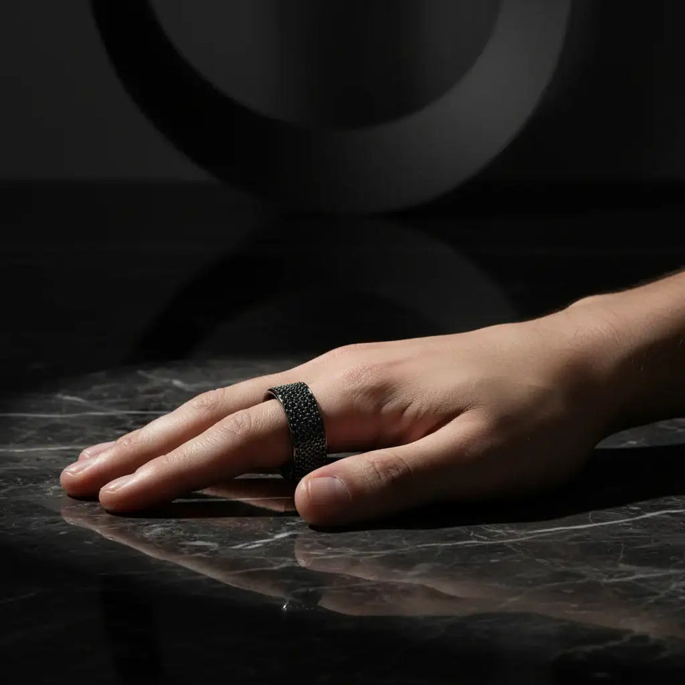 Angled view of a wide black rhodium–plated sterling silver band paved with black spinel stones