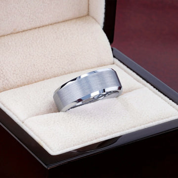 Close-up of the tungsten ring in a jewelry box, displaying the brushed center and reflective beveled sides