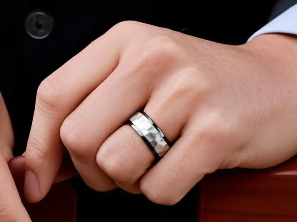 Lifestyle close-up of the black tungsten ring worn on a hand, showing the hammered white center and polished black beveled edges