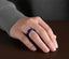 Black tungsten and blue ceramic T-link ring shown worn on hand against dark tabletop