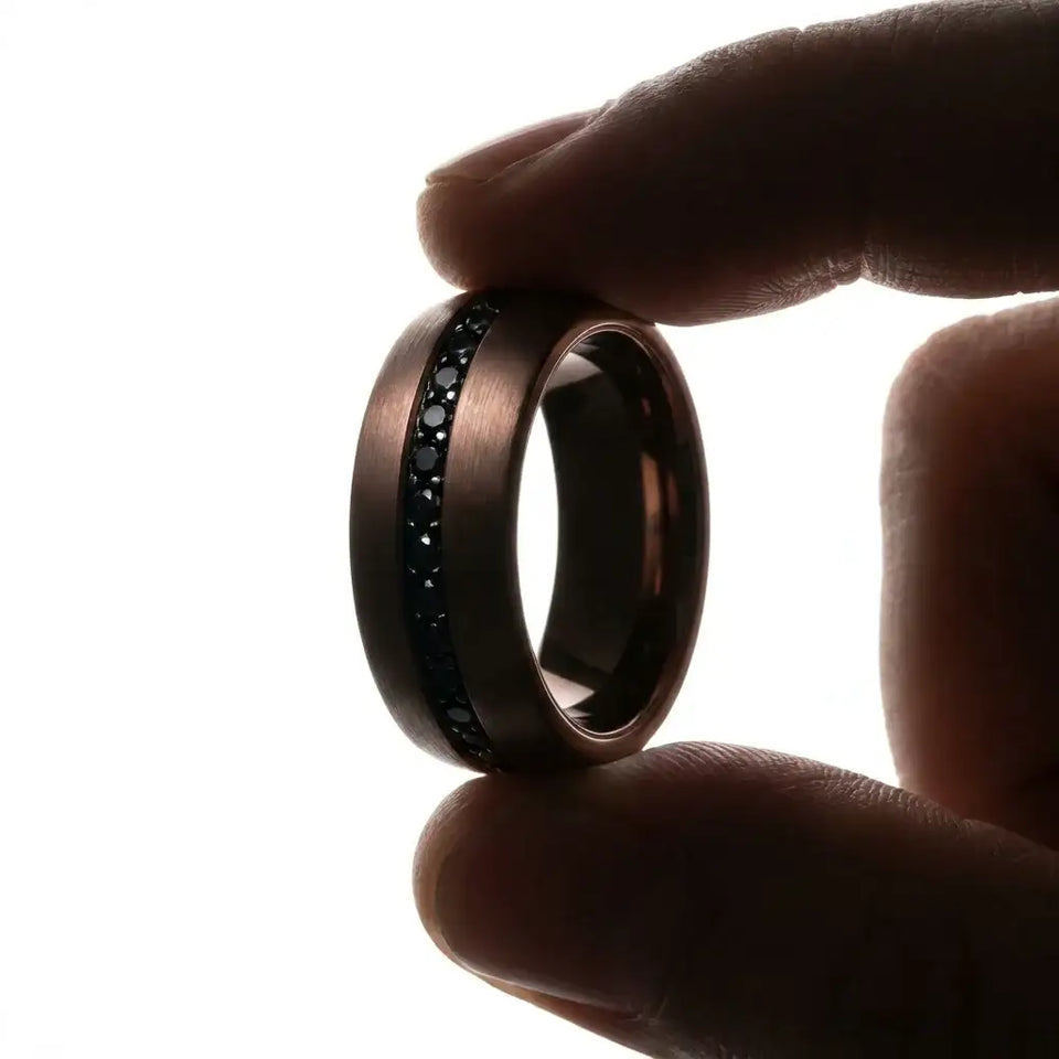 Dark tungsten carbide ring with black sapphires set in center band, held in hand against white background.