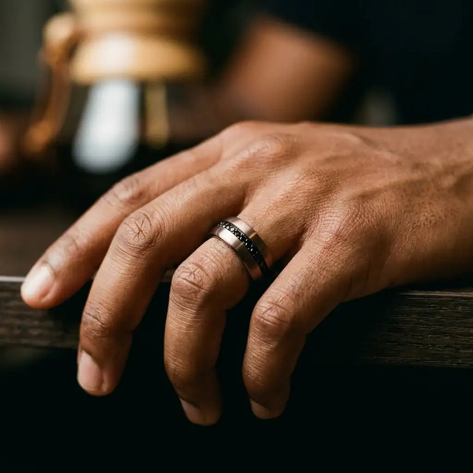 Dark tungsten carbide band with black stone inlays worn on man's hand.