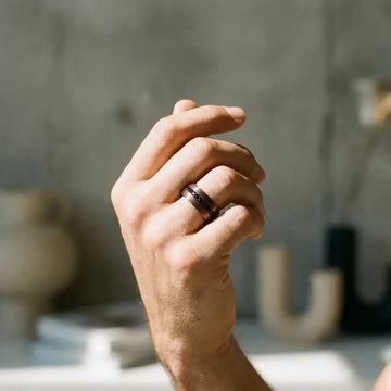 Dark tungsten carbide band with black stone inlays worn on ring finger of a man's hand.