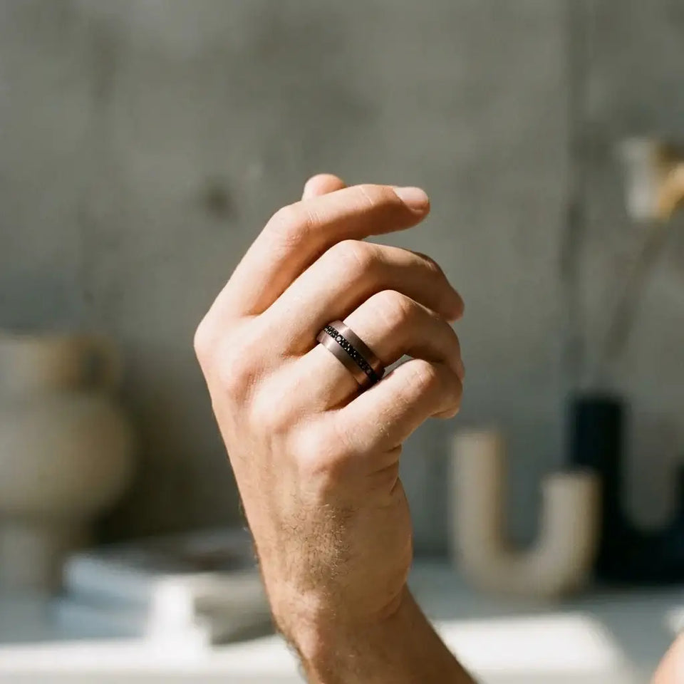 Dark tungsten carbide band with black stone inlays worn on ring finger of a man's hand.
