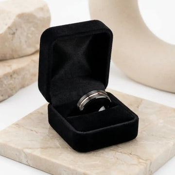 Black tungsten wedding band with flat brushed finish and dark center groove displayed in open black velvet box.