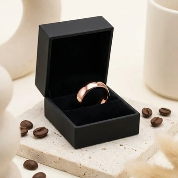 Rose gold domed tungsten carbide wedding ring displayed in black box with coffee beans nearby.