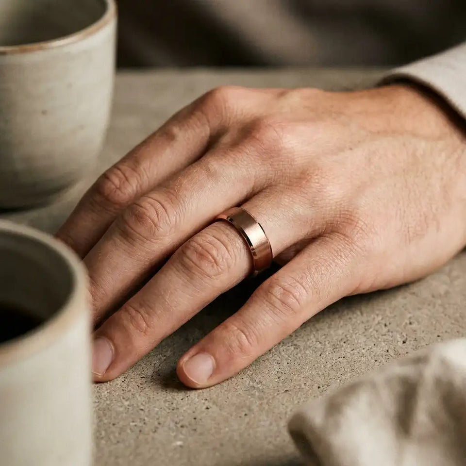 Two-tone tungsten carbide ring with flat beveled edges and brushed center band worn on person's hand next to ceramic cup.