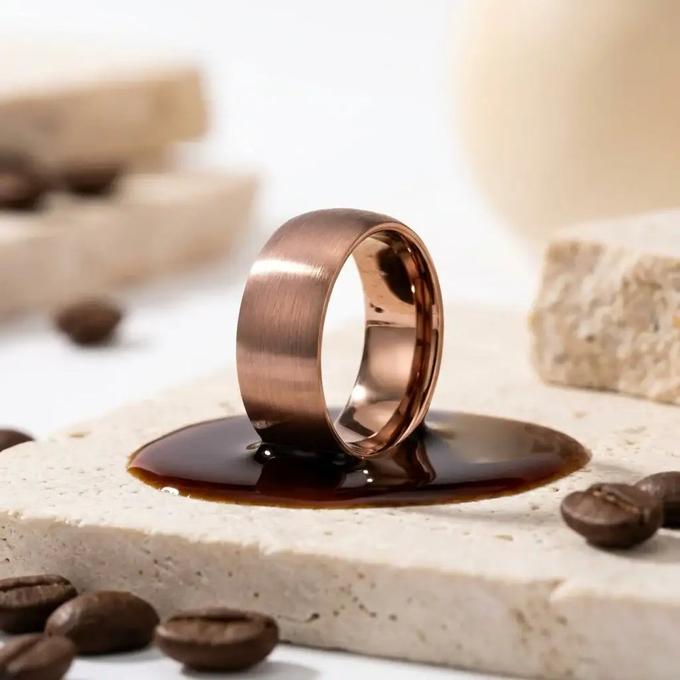 Domed espresso tungsten band ring with brushed finish on stone surface.
