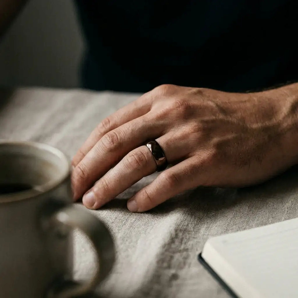 Dark brown domed wedding band on man's hand resting on fabric surface.