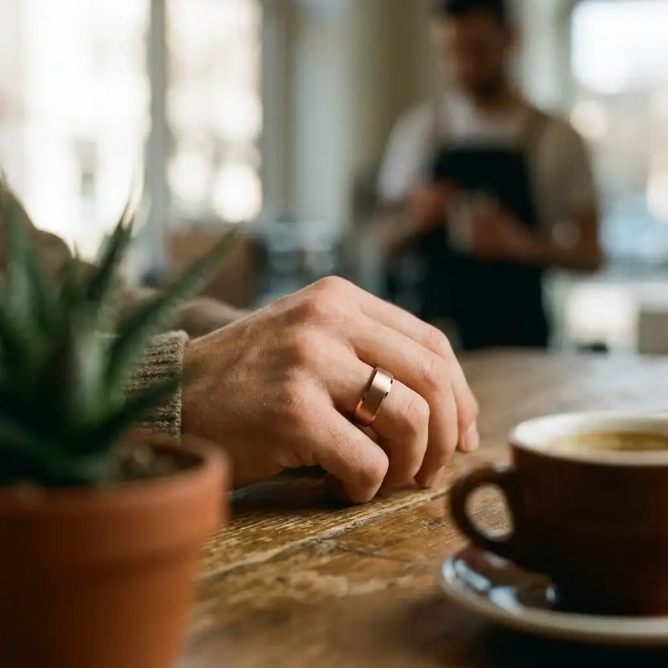 Gold tungsten carbide ring with brushed center and beveled edges worn on person's hand at table.
