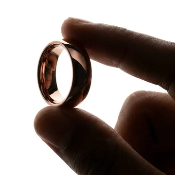 Polished coffee-brown domed tungsten carbide ring with high-shine finish held between fingers.