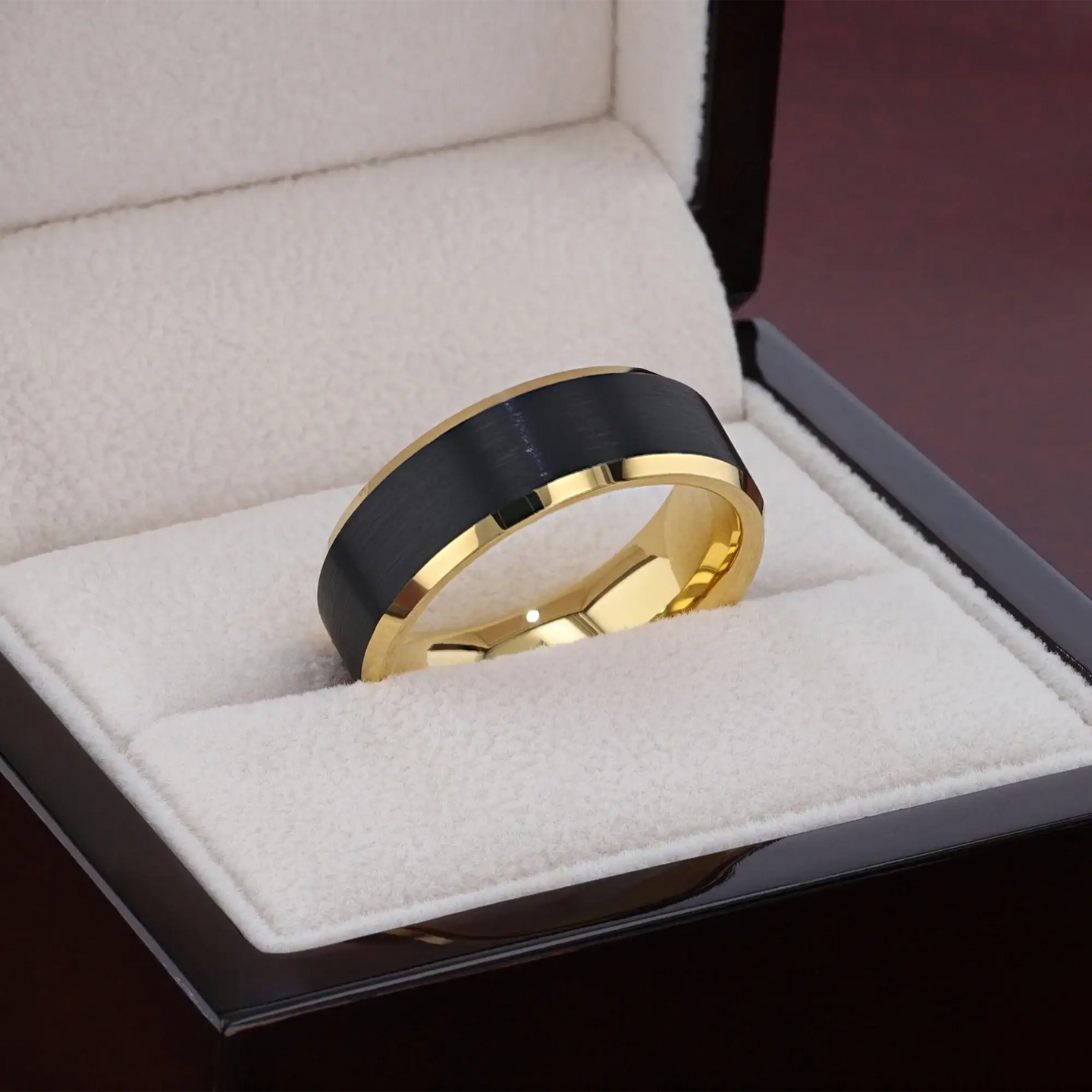 Ring standing upright on a tabletop with greenery, showing brushed black center and gold edges