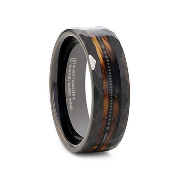 Angled view of an 8mm black tungsten ring with faceted hex-pattern edges, charred whiskey barrel wood inlay, and a centered guitar string