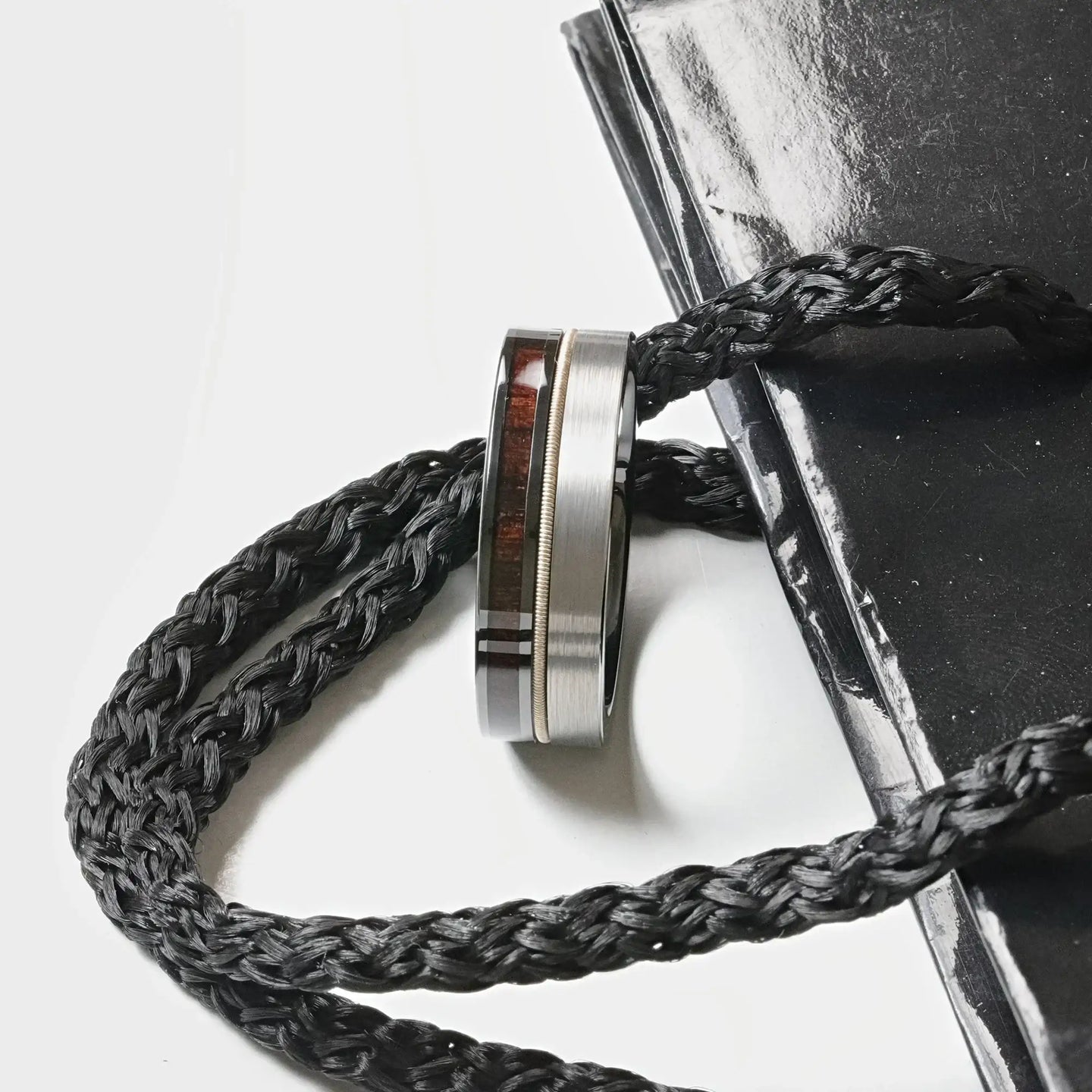 Lifestyle shot of the SLATE tungsten and black ceramic hybrid ring looped through a black braided cord beside a black notebook