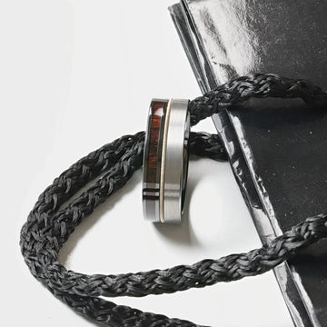 Lifestyle shot of the SLATE tungsten and black ceramic hybrid ring looped through a black braided cord beside a black notebook