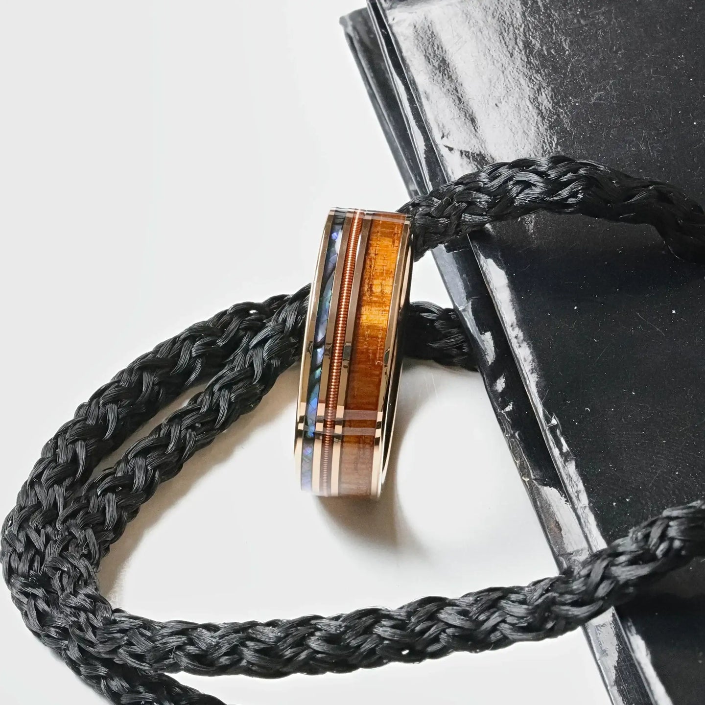 Angled lifestyle shot emphasizing the koa wood grain and abalone shell strip on the smoked rose gold tungsten ring