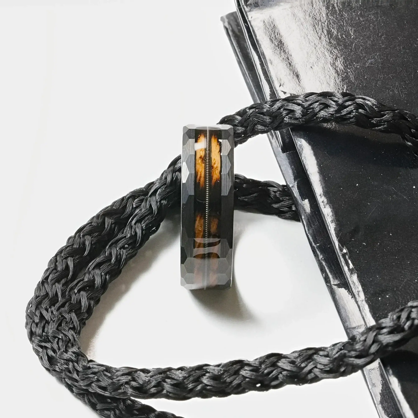 Lifestyle shot of the ring resting on braided black cord, showing the wood inlay and guitar string detail