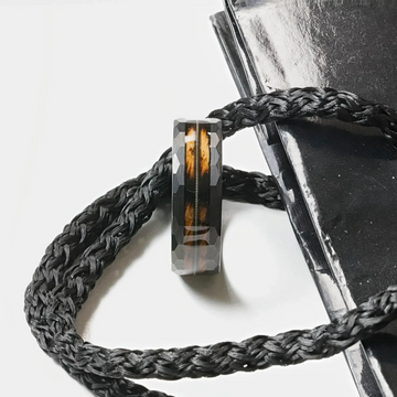 Lifestyle shot of the ring resting on braided black cord, showing the wood inlay and guitar string detail