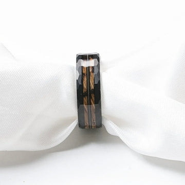 Close-up of the ring on white fabric, displaying the faceted black tungsten edges and center inlay