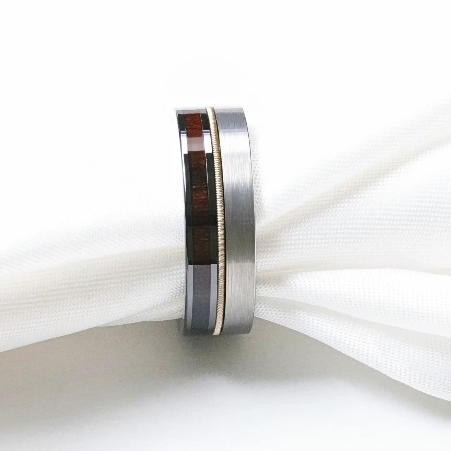 Close-up of the SLATE hybrid ring against white fabric, showing brushed tungsten exterior and ebony wood inlay